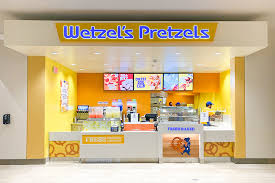 Store front photo of wetzels pretzels, featuring the cash register and menu board, along with menu food items on display.