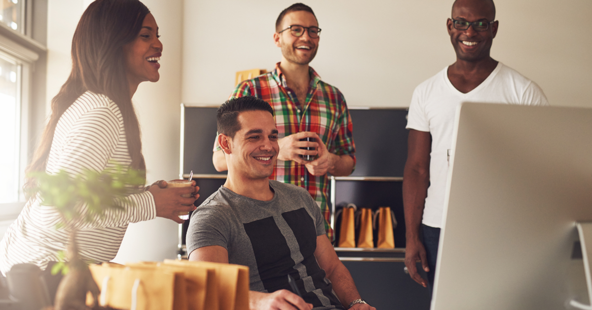 group of four friends surrounding a computer, smiling.
